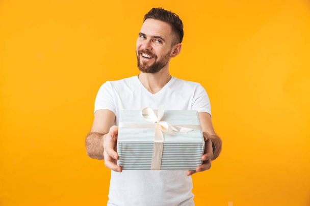 Man posing isolated over yellow wall background holding gift box. - Foto, Imagem
