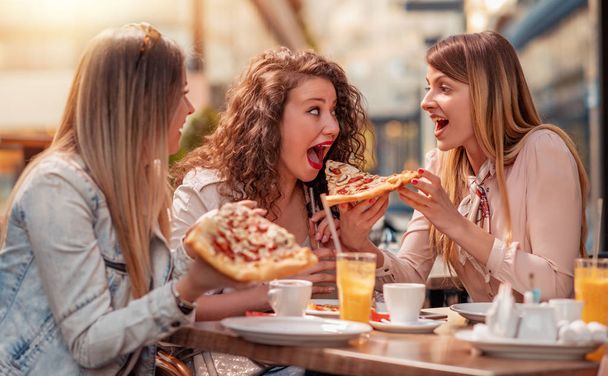 Tre ragazze allegre che mangiano pizza in un ristorante all'aperto. Concetto di persone, cibo, bevande e stile di vita
. - Foto, immagini