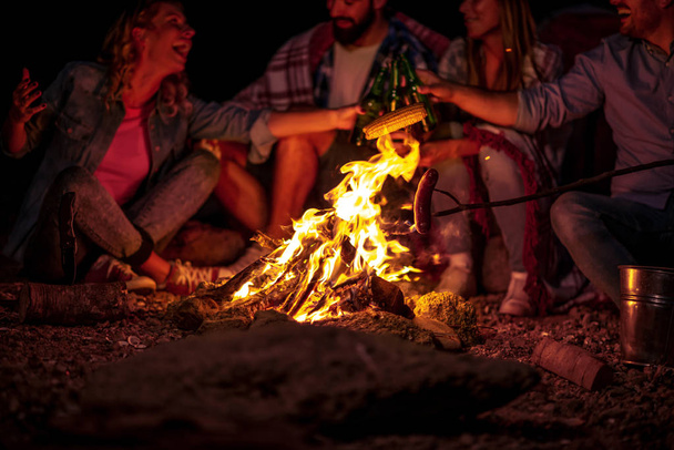 Amigos haciendo picnic alrededor del fuego. Grupo de jóvenes amigos haciendo picnic por la noche.  - Foto, imagen