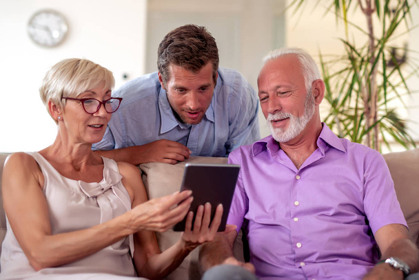 Senior couple with their son using digital tablet at home. - 写真・画像