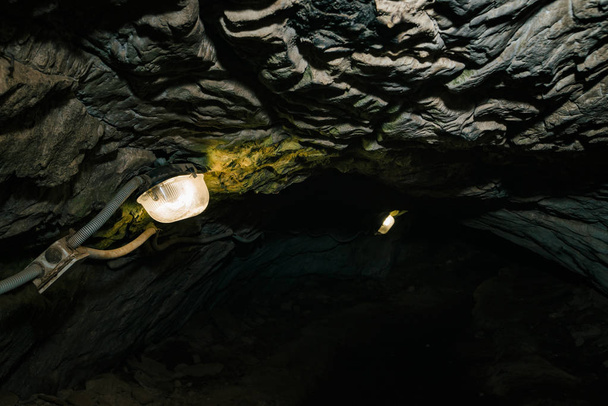 美しい洞窟だ暗いダンジョンの中からの眺め。洞窟のテクスチャードの壁。地下トンネルの背景画像。洞窟内の湿気。小旅行のための洞窟内の照明. - 写真・画像