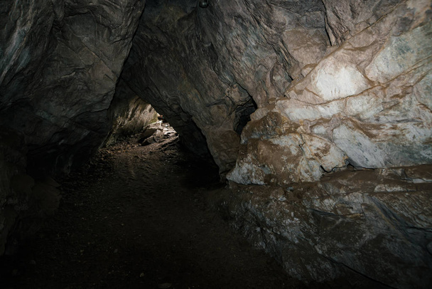 Beautiful cave. View from inside dark dungeon. Textured walls of cave. Background image of underground. Dampness inside cave. Light at end of tunnel. - Foto, Bild