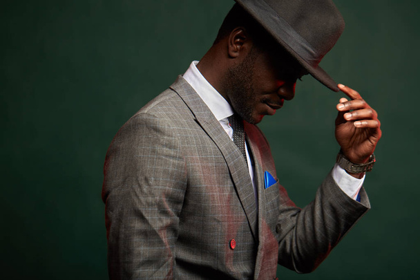 African businessman in grey suit and black hat in studio on dark background - 写真・画像
