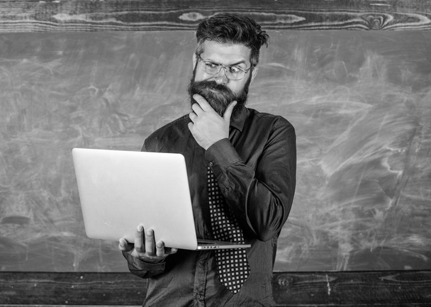 Distance education concept. Surfing internet. Hipster teacher wear eyeglasses and necktie holds laptop surfing internet. Teacher bearded man with modern laptop surfing internet chalkboard background - Photo, Image