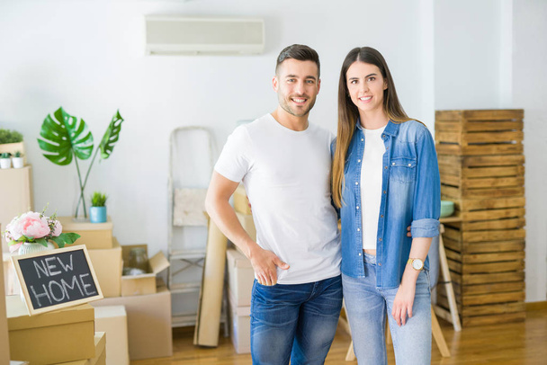 Belo jovem casal se mudando para uma nova casa, sorrindo felizes arround caixas de papelão
 - Foto, Imagem