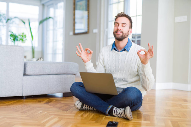 Beau homme portant le travail à l'aide d'un ordinateur portable se détendre et sourire les yeux fermés en faisant geste de méditation avec les doigts. Concept de yoga
. - Photo, image