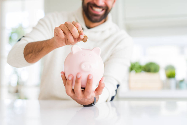Hombre sonriendo poniendo una moneda dentro de alcancía ahorro para invierte
 - Foto, Imagen