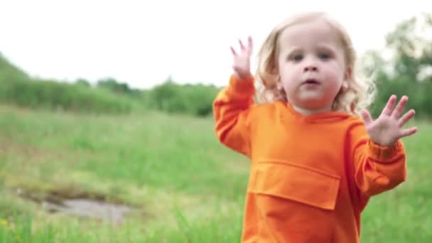 Μικρό αγόρι με πορτοκαλί φούτερ με κουκούλα τρέχει στο γρασίδι - Πλάνα, βίντεο