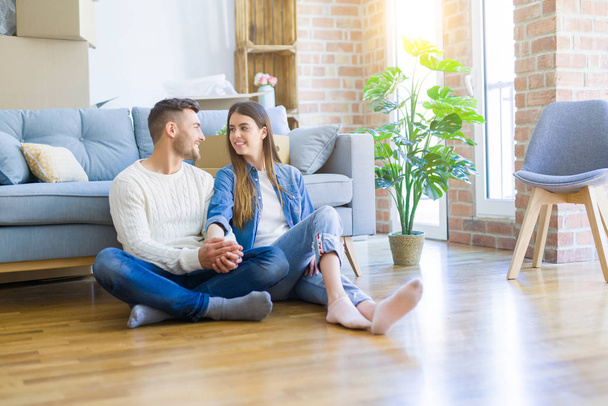 Молода красива пара сидить на підлозі нової квартири, посміхаючись в любові щаслива за переїзд в новий будинок
 - Фото, зображення