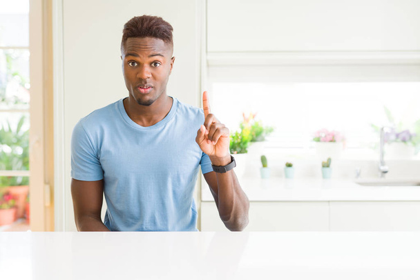 Bell'uomo afroamericano che indossa una maglietta casual a casa mostrando e indicando con il dito numero uno sorridendo fiducioso e felice
. - Foto, immagini