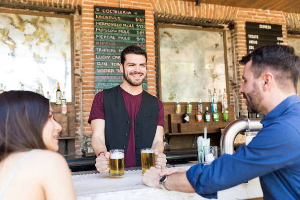 Happy bartender serving beer to customers at counter in bar - Foto, imagen