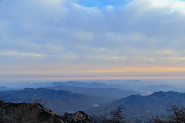 Το βουνό είναι κορυφαίο. Tai ' An, Κίνα-χειμώνας 2017: θέα από την κορυφή του βουνού Tai, την κορυφή του βουνού Tai. Βράχια και χιόνι στις κορυφές. Πεύκα στην κορυφή. Τα βουνά στην απόσταση έχουν ανθίσει. Τα σύννεφα το είχαν τυλιγμένο. Τα σύννεφα στον ουρανό ήταν πυκνά - Φωτογραφία, εικόνα