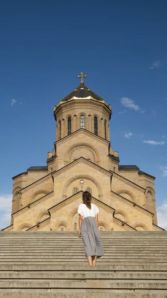 Ένα κορίτσι σε ένα μακρύ φόρεμα στέκεται στο φόντο ενός παλιού χριστιανικού ναού - Φωτογραφία, εικόνα