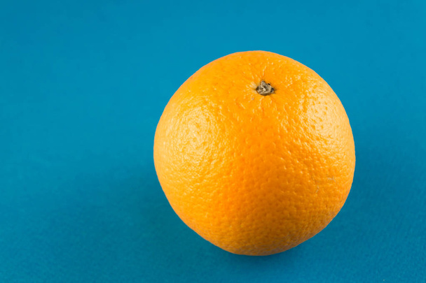 コピースペース付きの水色の背景に1つの鮮やかなオレンジ色のブラッドオレンジのクローズアップ - 写真・画像