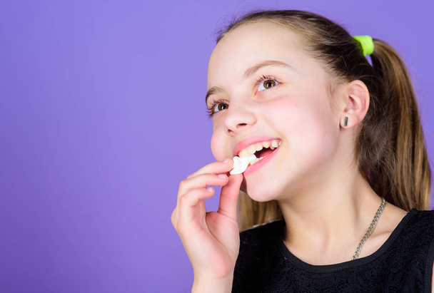Sweet tooth concept. Kid girl with long hair likes sweets and treats. Calorie and diet. Hungry kid. Incorrigible sweet tooth. Girl smiling face holds sweet marshmallows in hand violet background - Foto, imagen