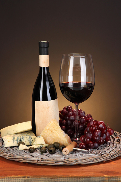 Refined still life of wine, cheese and grapes on wicker tray on wooden table on brown background - Fotografie, Obrázek