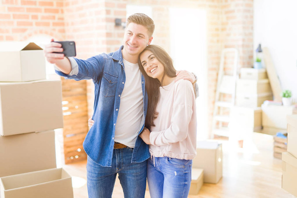 Hermosa pareja joven sonriendo feliz de tomar una foto selfie con el teléfono inteligente, muy emocionado de mudarse a un nuevo hogar
 - Foto, imagen