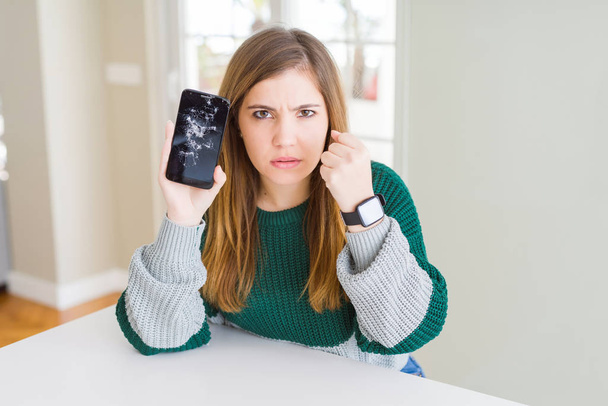 Hermosa mujer joven sosteniendo roto teléfono inteligente molesto y frustrado gritando con ira, loco y gritando con la mano levantada, concepto de ira
 - Foto, imagen