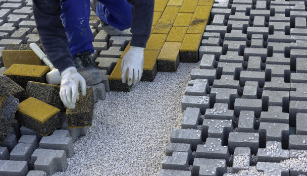 Paving stone worker is putting down pavers during a construction of a city street onto sheet nonwoven bedding sand and fitting them into place. - Photo, Image