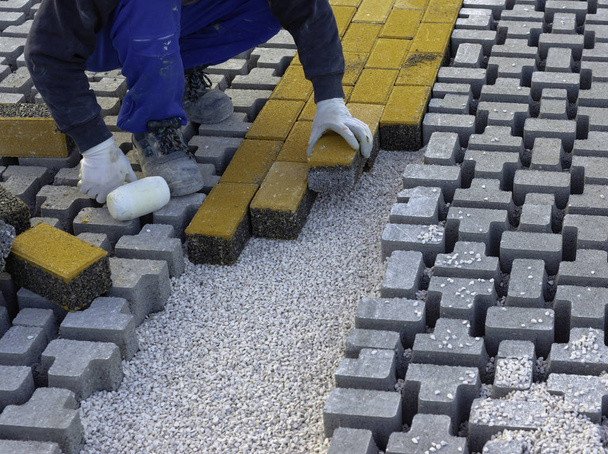 A kőmunkás járdákat tesz le egy városi utca építése során, lepedőre, nem szőtt ágyneműre, homokra, és a helyére szereli.. - Fotó, kép