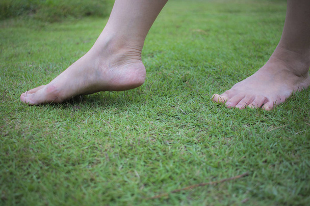 Nuoren naisen paljain jaloin kävelemässä tuoreella, vihreällä ruoholla auringossa
 - Valokuva, kuva