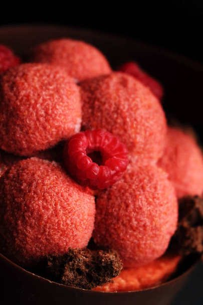 Duży czerwony deser malinowy ze świeżymi malinami i teksturowaną czekoladą z bliska na czarnym tle - Zdjęcie, obraz