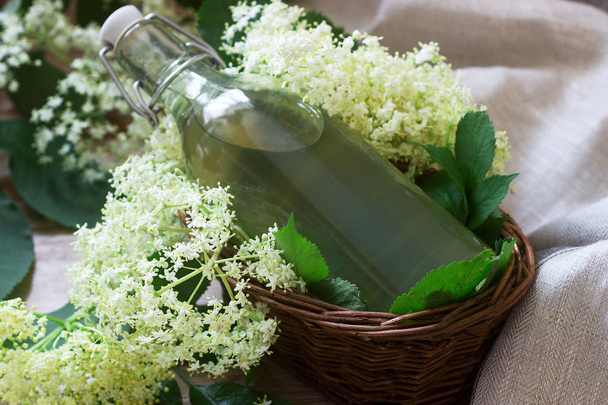Σπιτικά σιρόπι λουλουδιών σε ένα γυάλινο βάζο και γηραιότερος κλαδιά σε ένα ξύλινο τραπέζι ρουστίκ στυλ. - Φωτογραφία, εικόνα