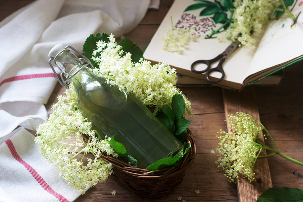 Σπιτικά σιρόπι λουλουδιών σε ένα γυάλινο βάζο και γηραιότερος κλαδιά σε ένα ξύλινο τραπέζι ρουστίκ στυλ. - Φωτογραφία, εικόνα