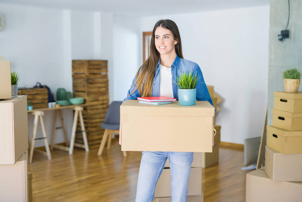Красива молода жінка тримає картонну коробку в новій квартирі, посміхаючись дуже щасливо переїжджаючи в новий будинок
 - Фото, зображення