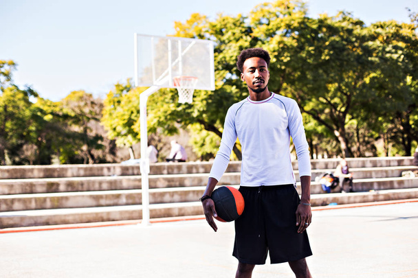 Young athletic black man posinging on court with ball, basketball game player, morning exercises, active healthy lifestyle, hot summer day, streetball. - Фото, зображення