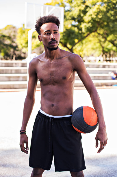Young athletic black man posinging on court with ball, basketball game player, morning exercises, active healthy lifestyle, hot summer day, streetball. - Valokuva, kuva