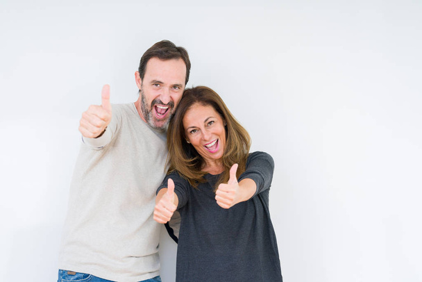 Beautiful middle age couple in love over isolated background approving doing positive gesture with hand, thumbs up smiling and happy for success. Looking at the camera, winner gesture. - Foto, Bild