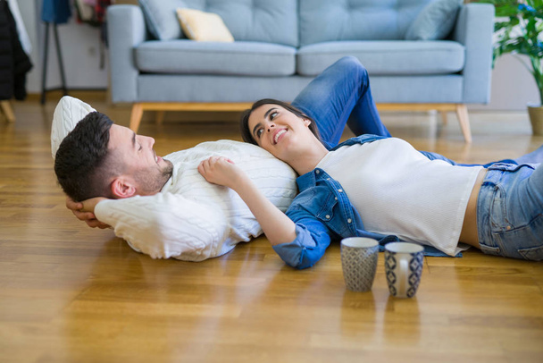 Joven hermosa pareja tumbada en el suelo de la nueva casa, sonriendo en el amor muy feliz por mudarse a un nuevo apartamento
 - Foto, Imagen