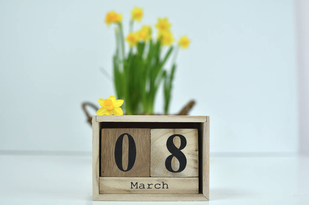 8 March composition on white background. March 8 text on wooden block calendar and one flower of yellow narcissus .basket of daffodils in the background - Photo, Image