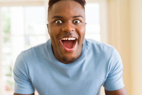 Афроамериканец кричит очень взволнованный и празднует успех и победу, улыбаясь счастливой и веселой
 - Фото, изображение