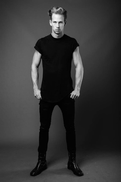 Studio shot of young handsome man wearing black shirt against gray background in black and white - Foto, immagini