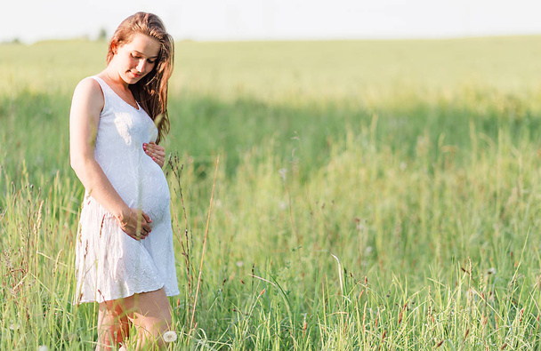 Gyönyörű terhes nő, fehér ruhában a réten - Fotó, kép