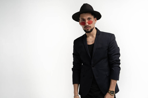 Cheerful confident young bearded man in black suit and hat in red sunglasses isolated over white background - Photo, Image