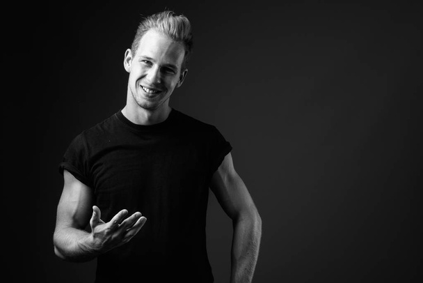 Studio shot of young handsome man wearing black shirt against gray background in black and white - Foto, afbeelding