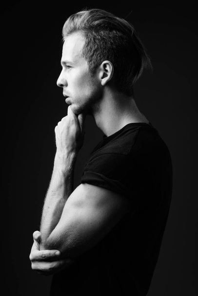 Studio shot of young handsome man wearing black shirt against gray background in black and white - Foto, Imagen