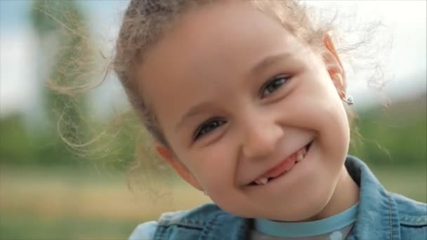 Közelről portré aranyos boldog kaukázusi kislány mosolygott keresi a kamera, élvezve meleg nyári vakáció napsütéses nap. - Felvétel, videó