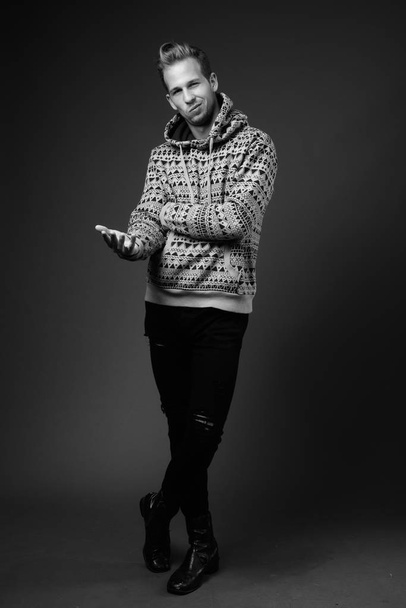 Studio shot of young handsome man wearing hoodie against gray background in black and white - Foto, Imagem