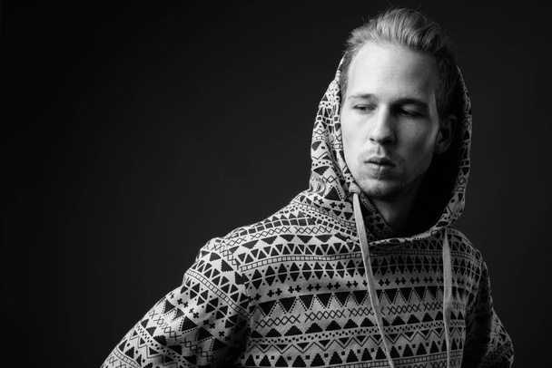 Studio shot of young handsome man wearing hoodie against gray background in black and white - Foto, afbeelding