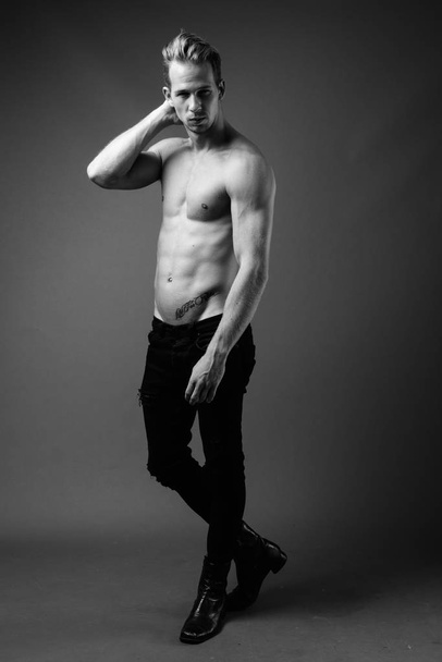 Studio shot of young handsome man shirtless against gray background in black and white - Photo, Image