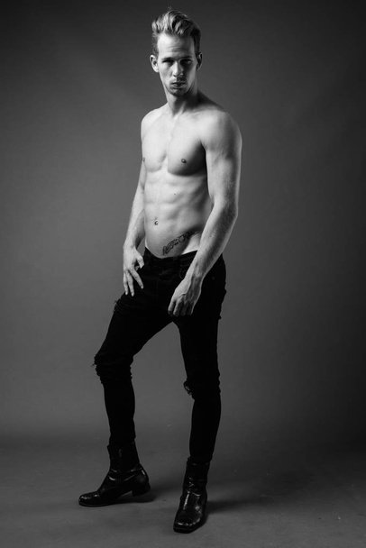 Studio shot of young handsome man shirtless against gray background in black and white - Fotó, kép