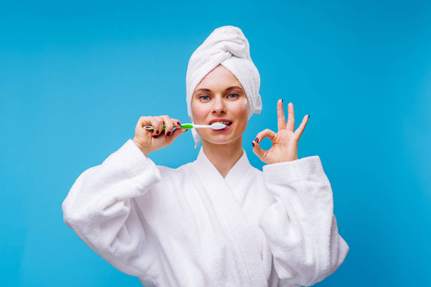 Picture of woman in white coat and towel on head brushing her teeth - Foto, Imagen