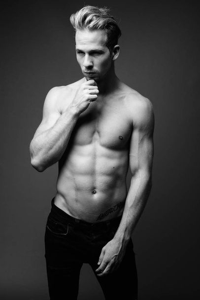 Στούντιο πλάνο του νεαρού όμορφου άνδρα shirtless σε γκρι φόντο σε μαύρο και άσπρο - Φωτογραφία, εικόνα