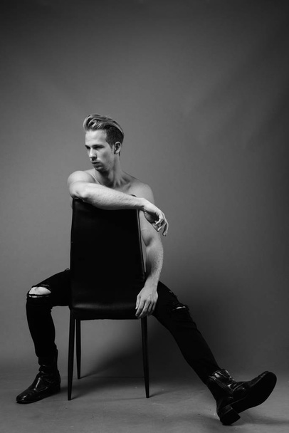 Στούντιο πλάνο του νεαρού όμορφου άνδρα shirtless σε γκρι φόντο σε μαύρο και άσπρο - Φωτογραφία, εικόνα