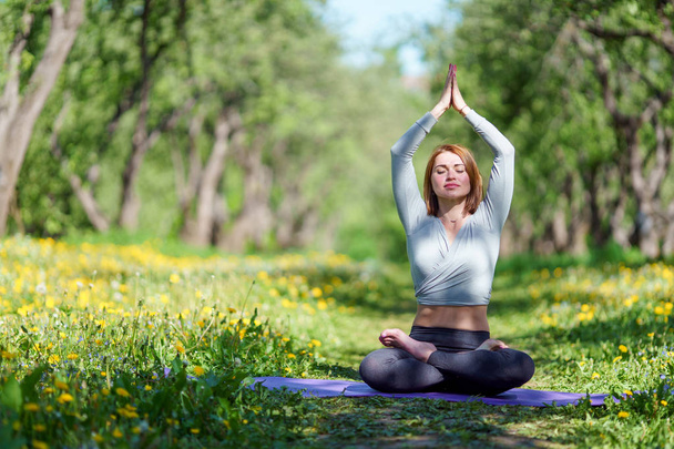 Photo of woman doing yoga with arms raised sitting in lotus position on blue rug in forest - Photo, Image