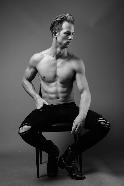 Studio shot of young handsome man shirtless against gray background in black and white - Foto, Imagen